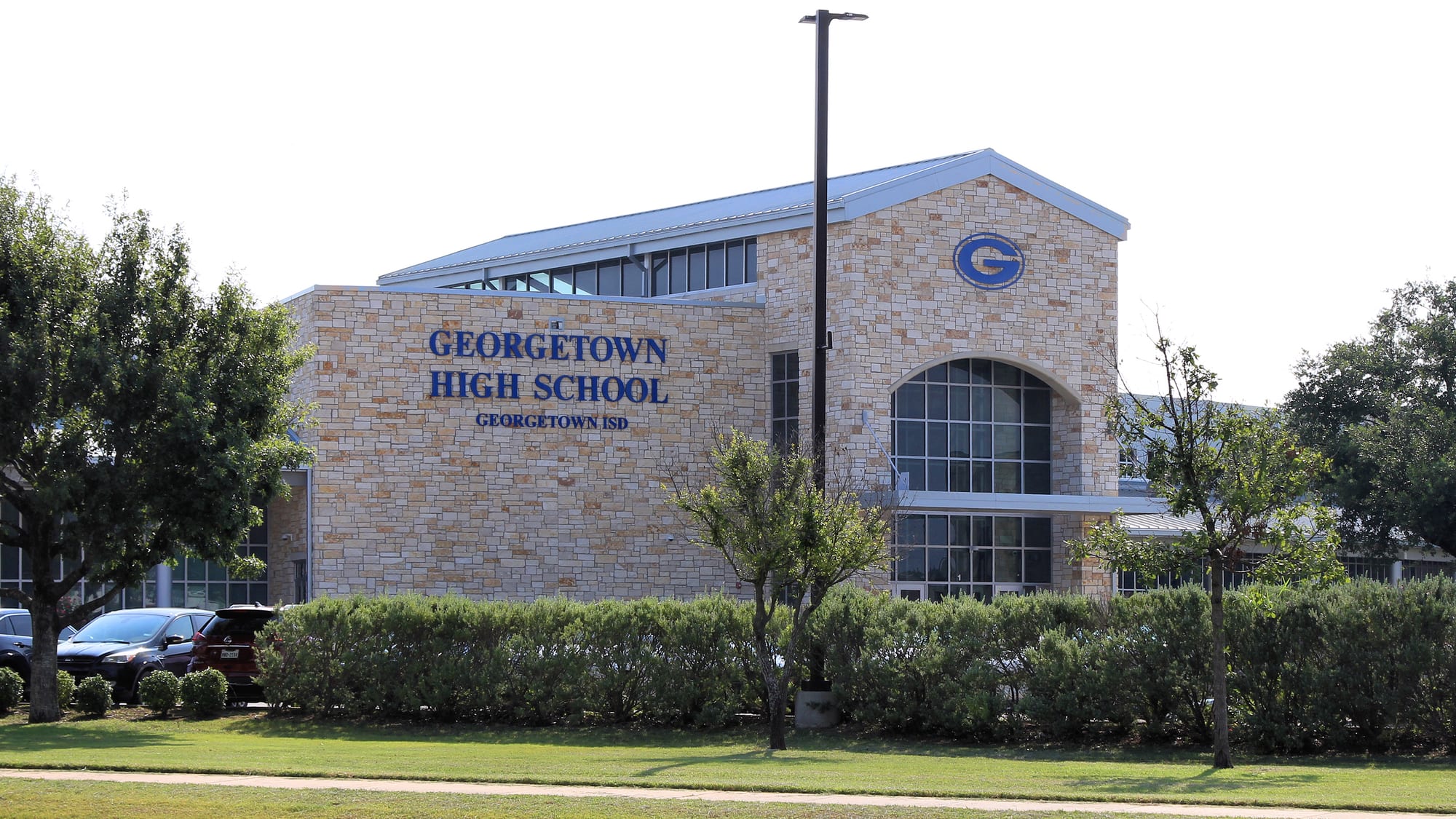 Limestone front entrance of Georgetown High School with the Georgetown ISD name and logo, framed by trees and hedges